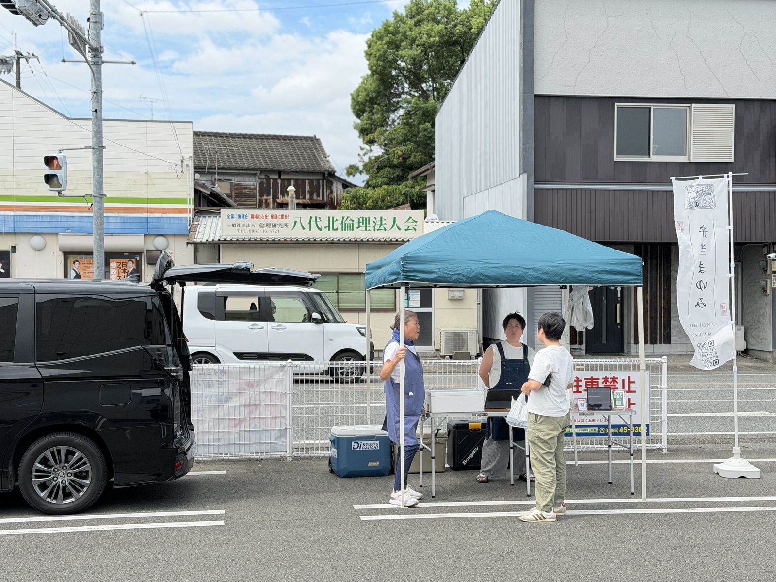 鏡町の販売所。テントの下でお弁当を手渡す2人